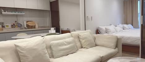 A modern hotel room with a sofa, a round marble table, a bed, and a kitchen area.