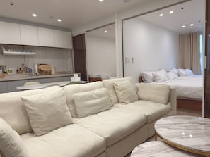 A modern hotel room with a sofa, a round marble table, a bed, and a kitchen area.