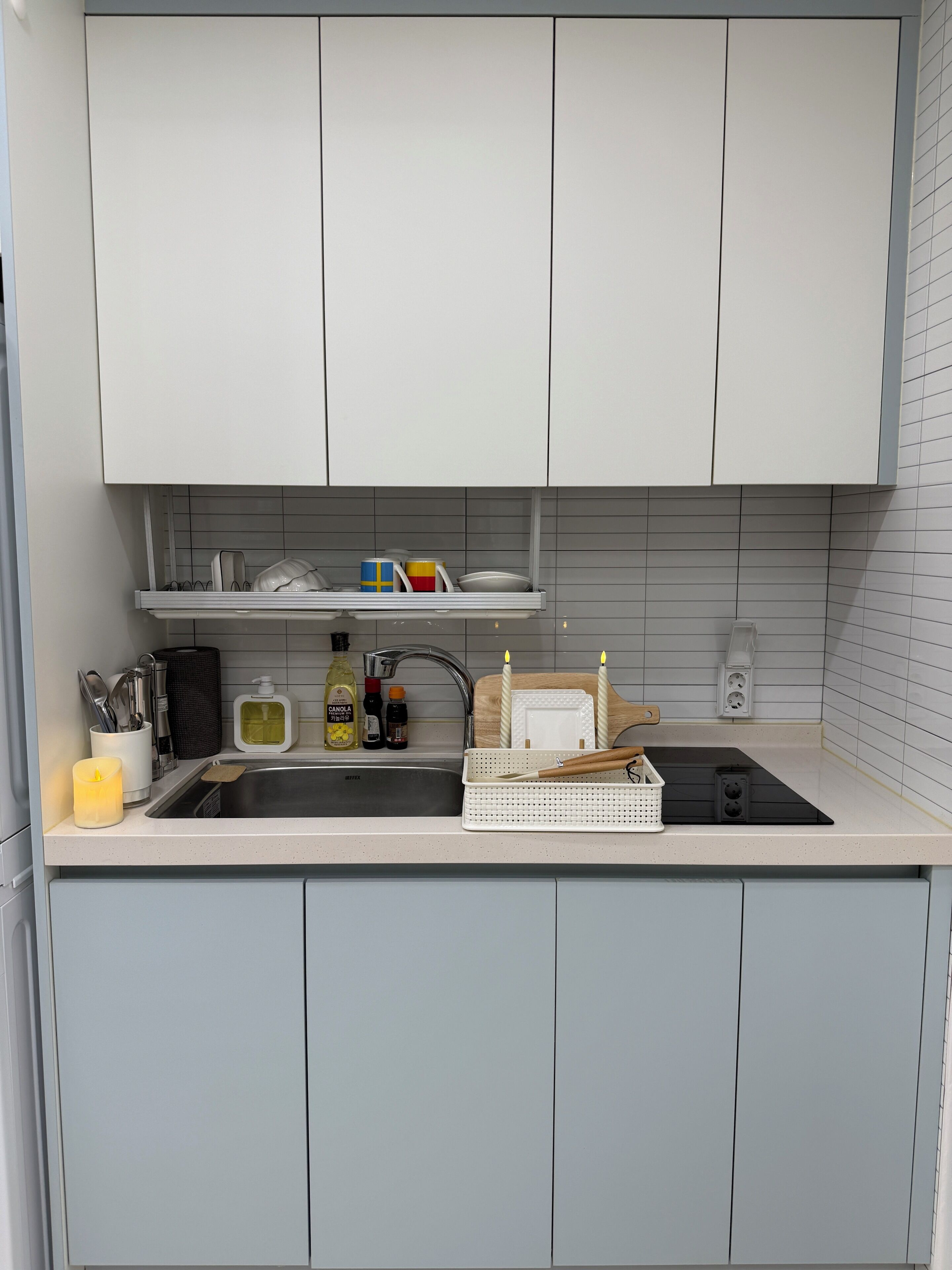A kitchen with white cabinets, a sink, a stove, and various kitchen items like a coffee maker, utensils, and a candle.