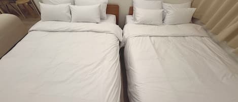 Two single beds with white linens and pillows, wooden headboards, and a small table with chairs in the background.