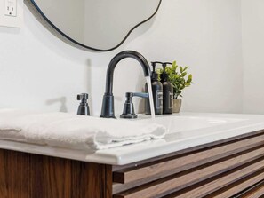 Ein Badezimmer mit einem weißen Waschbecken, einem schwarzen Wasserhahn und einem Spiegel darüber.
