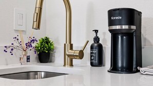 Una cocina moderna con un grifo dorado, una cafetera negra y una planta en maceta sobre la encimera.
