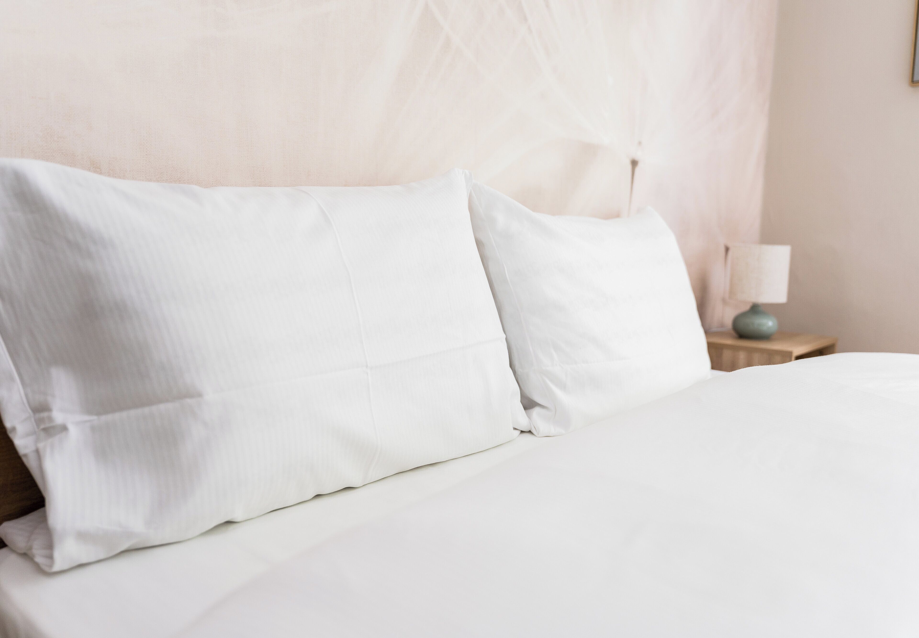 A neatly made bed with white bedding and pillows, a bedside table with a lamp, and a wall with a textured pattern.