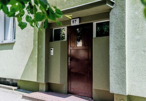 Entrada de un edificio con una puerta marrón, un cartel con el número 87 arriba y una ventana a la izquierda.