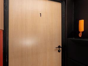 A wooden door with a black frame, a small number '1' on the door, a black door handle, and a yellow telephone on a black wall.