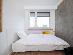 A bedroom with a bed, a window with blinds, a radiator, and a concrete wall. - Lermontowa Comfort Room #2 (Łódź)