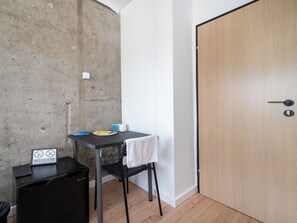 A small room with a concrete wall, a wooden door, a small table with a towel, a black chair, and a trash bin. - Lermontowa Comfort Room #2 (Łódź)