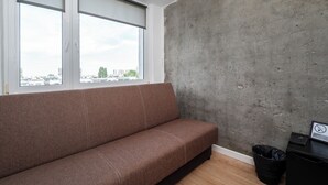 Ein modernes Zimmer mit einer braunen Couch, einer Wand mit Betonelementen und Blick auf Gebäude durch große Fenster.