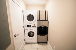 Une petite buanderie équipée d’un lave-linge et d’un sèche-linge à chargement frontal, d’un appareil à glaçons intégré et d’un distributeur de glaçons à bouton-poussoir.