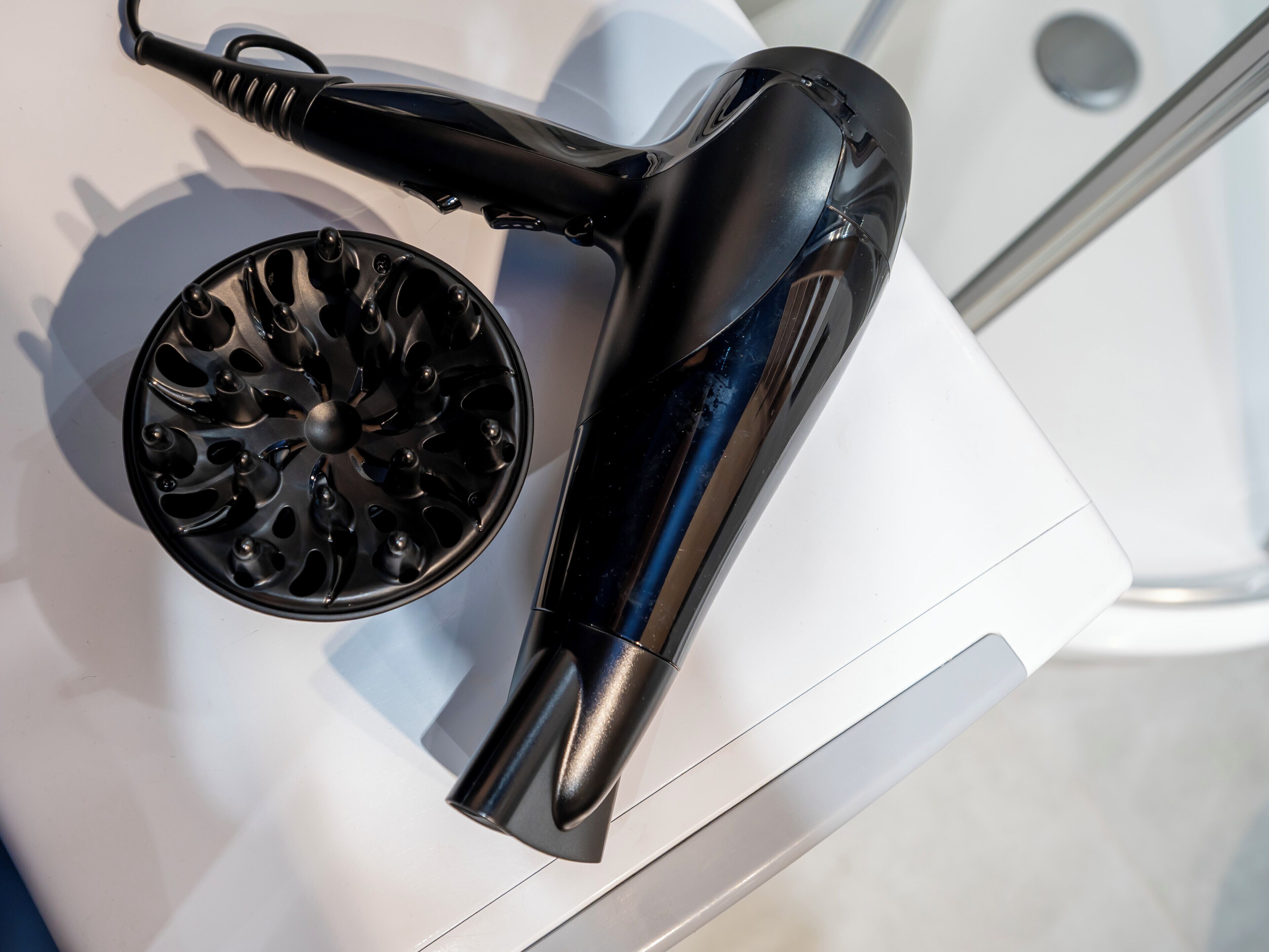 A black hairdryer and a black hairbrush on a white surface.