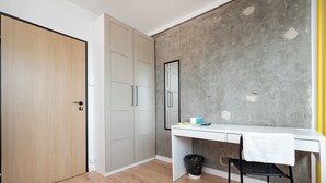 A room with a wooden floor, a white desk, a black chair, a white cabinet, and a concrete wall. - Lermontowa Comfort Room #3 (Łódź)