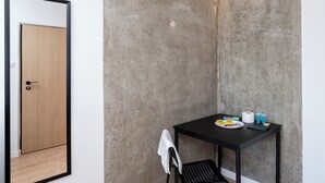 Une chambre d’angle avec une porte en bois, une table en métal noir sur laquelle sont posés des articles de toilette, et une chaise noire.