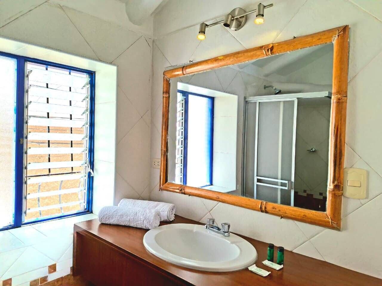 A bathroom with a large mirror, a sink, and a window with blinds.
