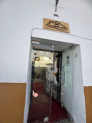 Una puerta con un letrero que dice 'Cusi Guest House' y un pequeño jardín visible a través del vidrio.