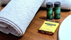 A bathroom with a white towel, two green bottles, and a yellow bar soap on a wooden surface. - Cusi Guest House (Cusco)
