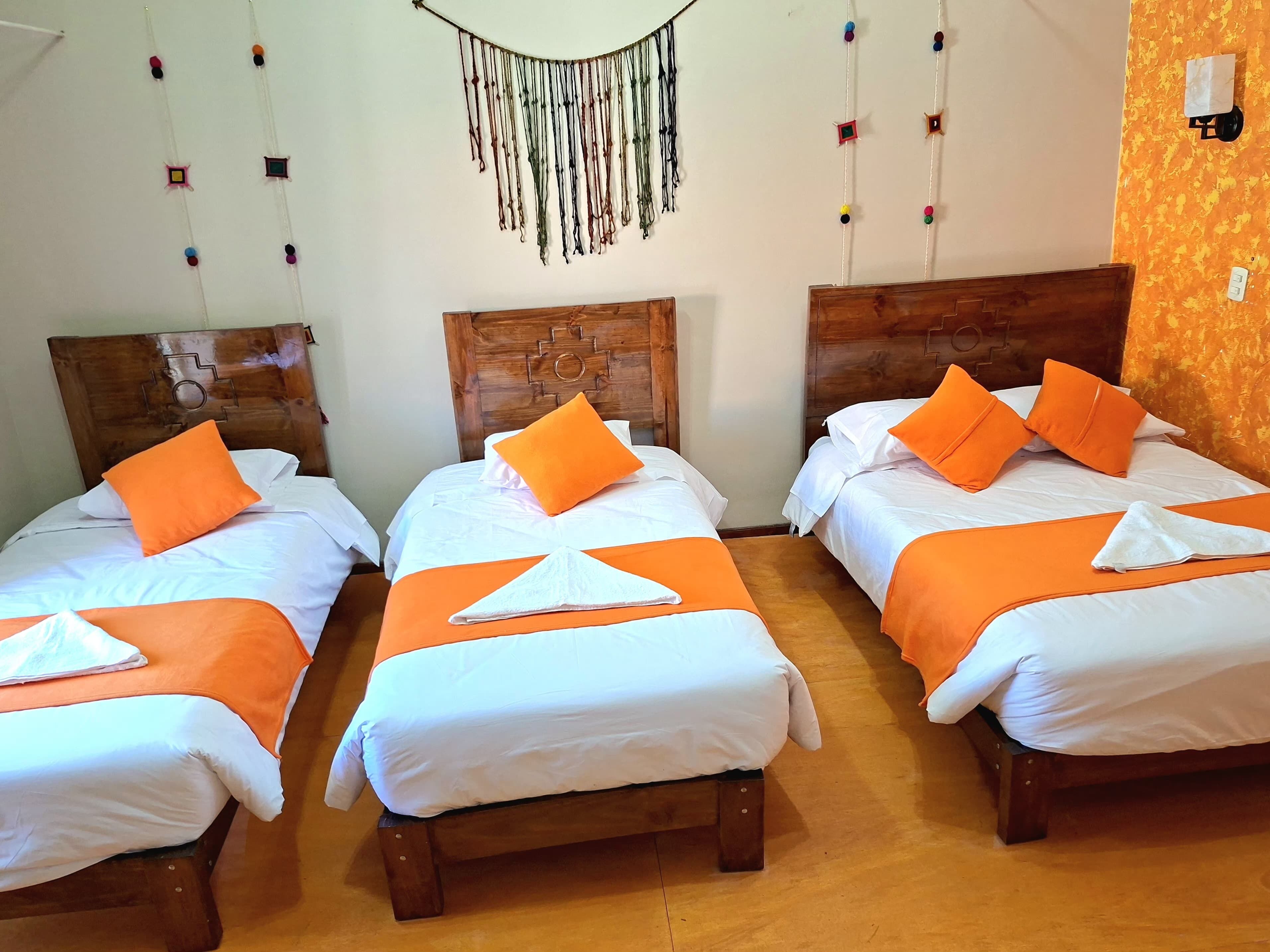 Three single beds with wooden headboards, white bedding, and orange pillows.