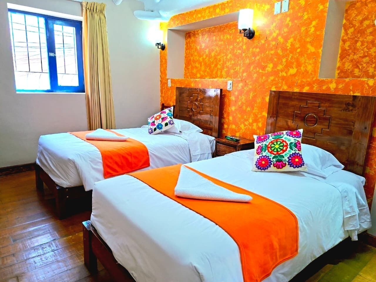 A hotel room with two beds, a window with curtains, and a wooden headboard.