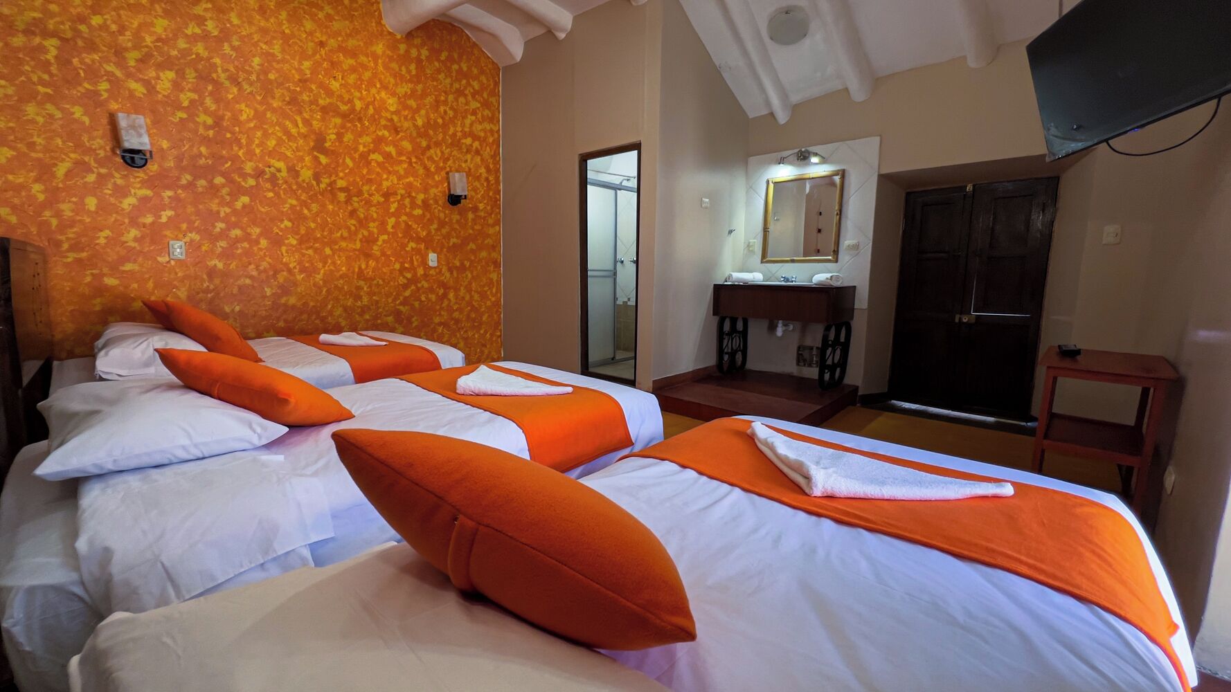 A hotel room with four beds, a wooden desk, a mirror, and a door.