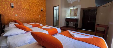 A hotel room with four beds, a wooden desk, a mirror, and a door.