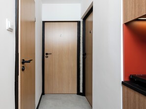 A hallway with a wooden door, a black door frame, a white wall, and a red accent wall. - Lermontowa Comfort Room #5 (Łódź)