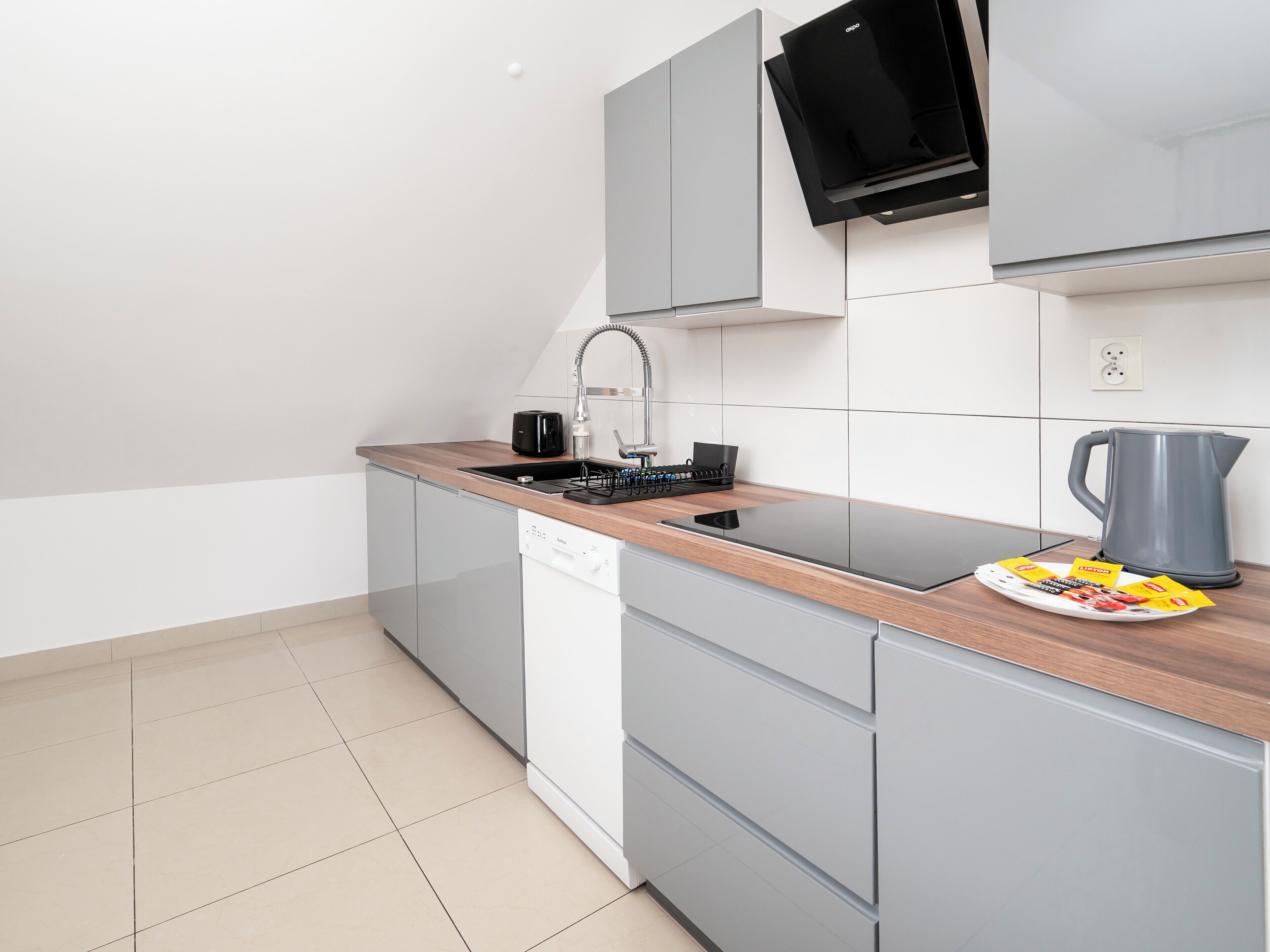 A modern kitchen with grey cabinets, a wooden countertop, a black coffee maker, a kettle, and a plate with food items.