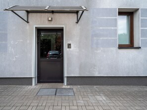 A building entrance with a black door, a small window, and a metal awning. - Stawy Jana Apartment #14 (Łódź)