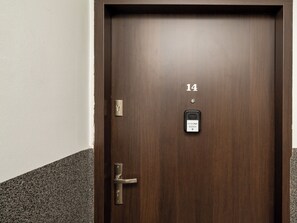 Una porta de fusta fosca amb un teclat numèric, una clau i un petit dispositiu electrònic amb pantalla.