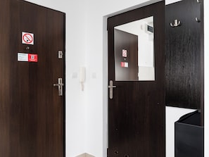 Zwei dunkle Holztüren mit einem Schild ‚kein Schlüsselloch‘, eine weiße Wand, ein weißes Klingelschild und ein kleiner Spiegel.