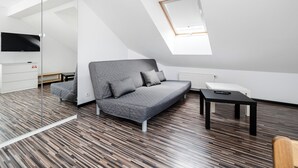 Ein modernes Schlafzimmer im Loft-Stil mit schrägverdeckter Decke, einem grauen Sofa, einem kleinen Tisch und einem an der Wand befestigten Fernseher.
