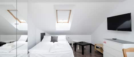 A modern hotel room with a large bed, a desk, a TV, and a skylight.