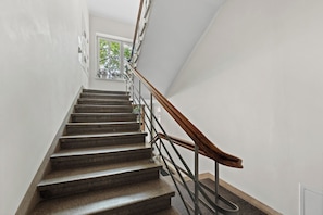 Eine Treppe mit hölzernem Geländer und Metallspindeln, die zu einer Zwischenebene mit einem Fenster führt.