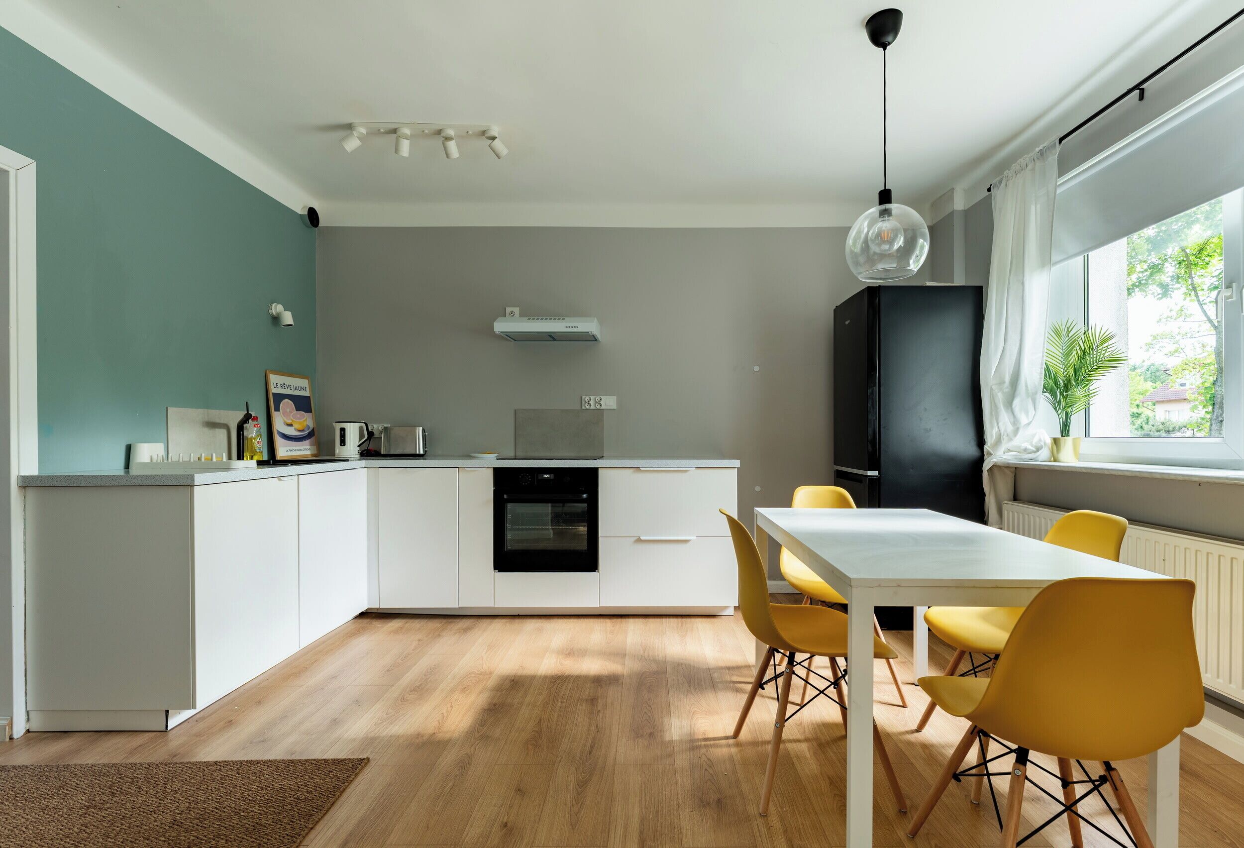 Une cuisine moderne avec des meubles blancs, un four encastré et un coin repas comprenant une table blanche et des chaises jaunes.