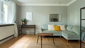 A living room with a sofa, a coffee table, a radiator, a plant, a framed picture, and a mirror on the wall. - Zielona Peaceful Apartment (Gdynia)