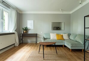 Ein Wohnzimmer mit einer Couch, einem Couchtisch, einem Heizkörper, einer Pflanze, einem gerahmten Bild und einem Spiegel an der Wand.