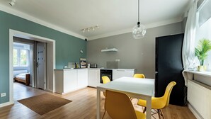 A modern kitchen with white cabinets, a black refrigerator, and a dining area with a white table and yellow chairs. - Zielona Peaceful Apartment (Gdynia)
