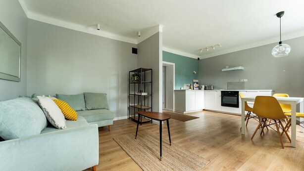 A modern living room with a sofa, a coffee table, and a dining area with chairs. - Zielona Peaceful Apartment (Gdynia)