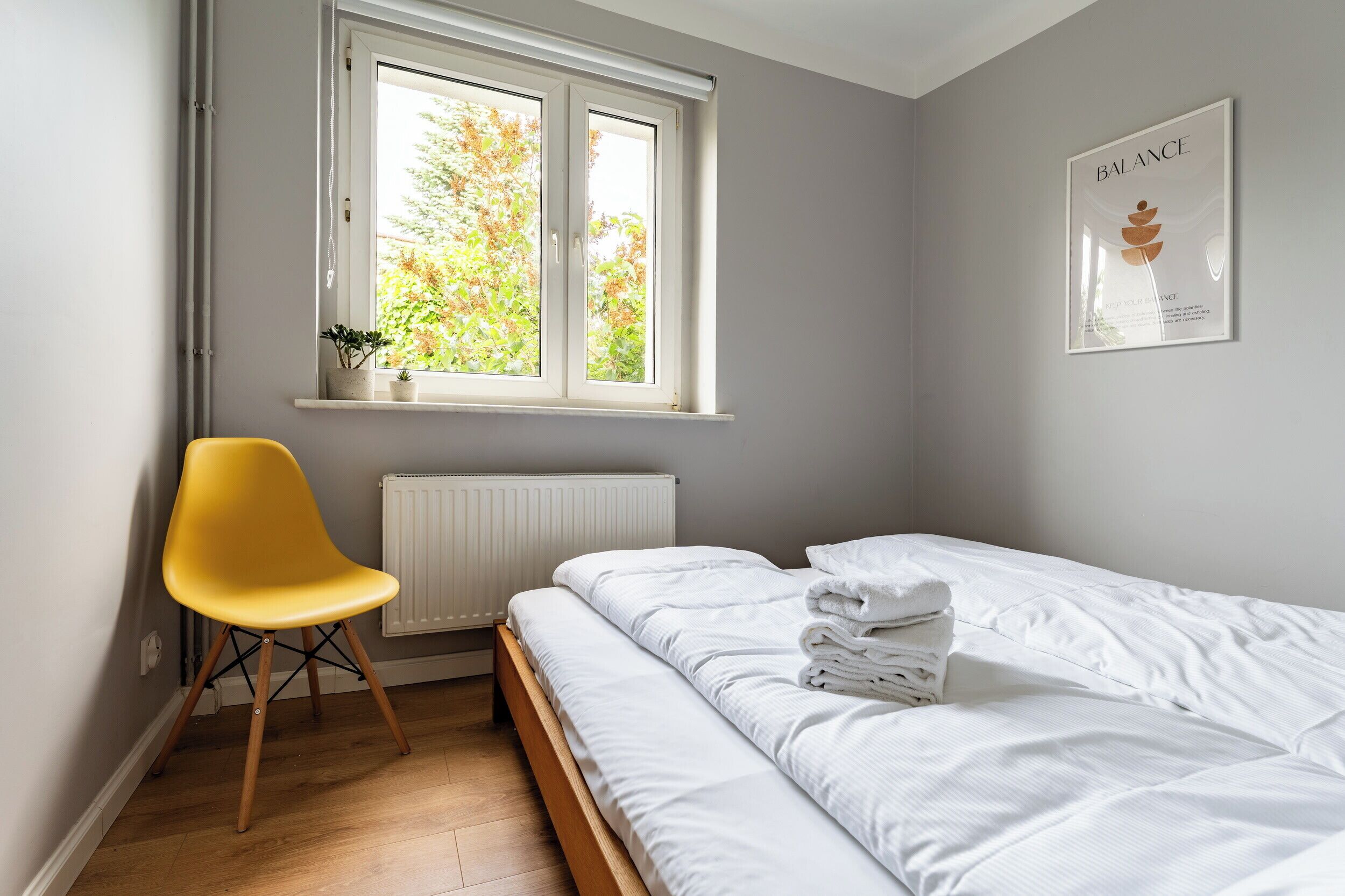 A bedroom with a bed, a chair, a window, a radiator, and a wall-mounted picture.