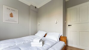 A neatly made bed with white linens and a folded towel, a white door, and a wall-mounted light fixture. - Zielona Peaceful Apartment (Gdynia)