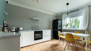 A modern kitchen with white cabinetry, a black refrigerator, and a dining area with yellow chairs. - Zielona Peaceful Apartment (Gdynia)