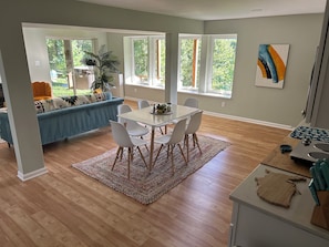 A modern kitchen with a dining area, large windows, and a view of greenery.