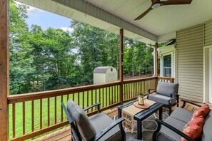 A covered porch with outdoor furniture, a small table, and a view of a yard and trees. - The Basecamp on Slaggford | B Home NWA (Bella Vista)