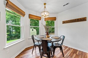 A dining area with a round table, chairs, a chandelier, and a sign reading 'The Gathering Place'. - The Basecamp on Slaggford | B Home NWA (Bella Vista)