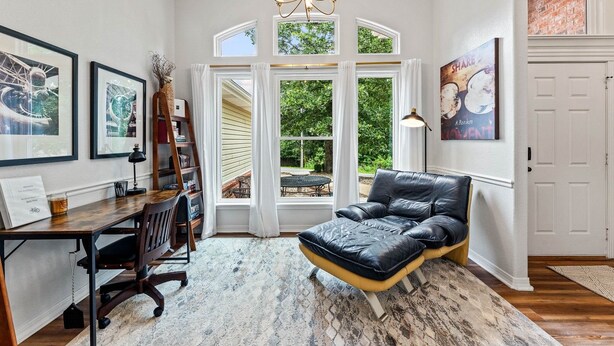 Una habitación con escritorio, silla, sofá de cuero negro, ventanas amplias y obras de arte.