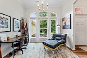A room with a desk, chair, black leather sofa, large windows, and artwork. - The Basecamp on Slaggford | B Home NWA (Bella Vista)