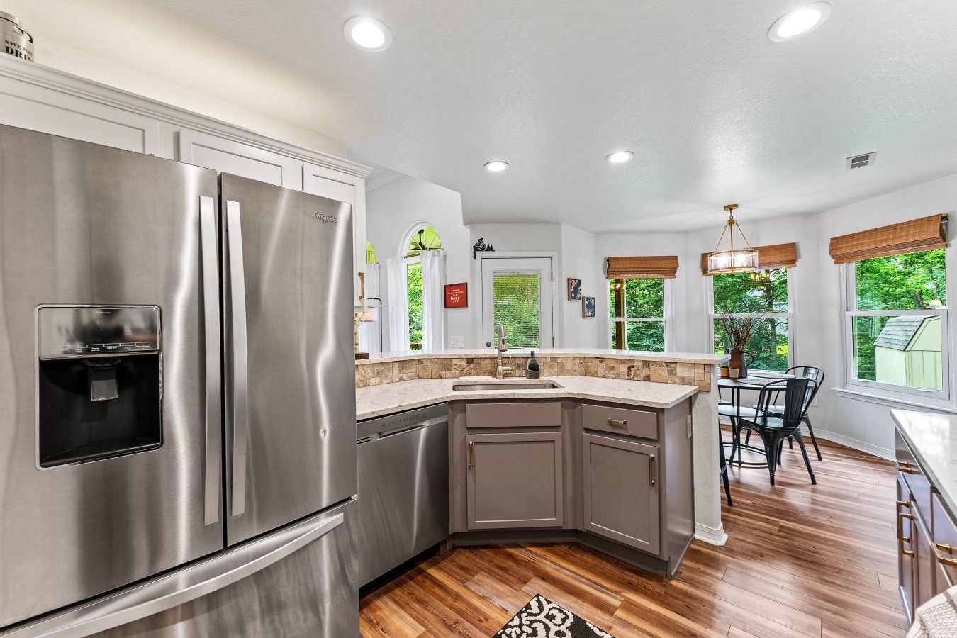 A modern kitchen with stainless steel appliances, a granite countertop, and a dining area with a view of greenery.