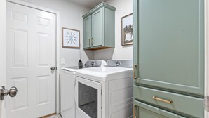 Un cuarto de lavandería con lavadora y secadora, un armario con tiradores dorados y una puerta con pomo.