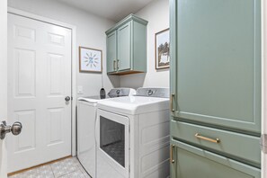 A laundry room with a washing machine and dryer, a cabinet with gold handles, and a door with a doorknob.