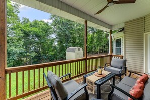 Une véranda aménagée avec du mobilier d’extérieur, une petite table et une vue sur une cour et des arbres.