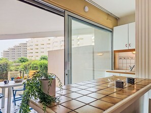 Een moderne keuken met een schuifdeur van glas, een betegelde spatwand en een klein aanrecht met twee mokken.
