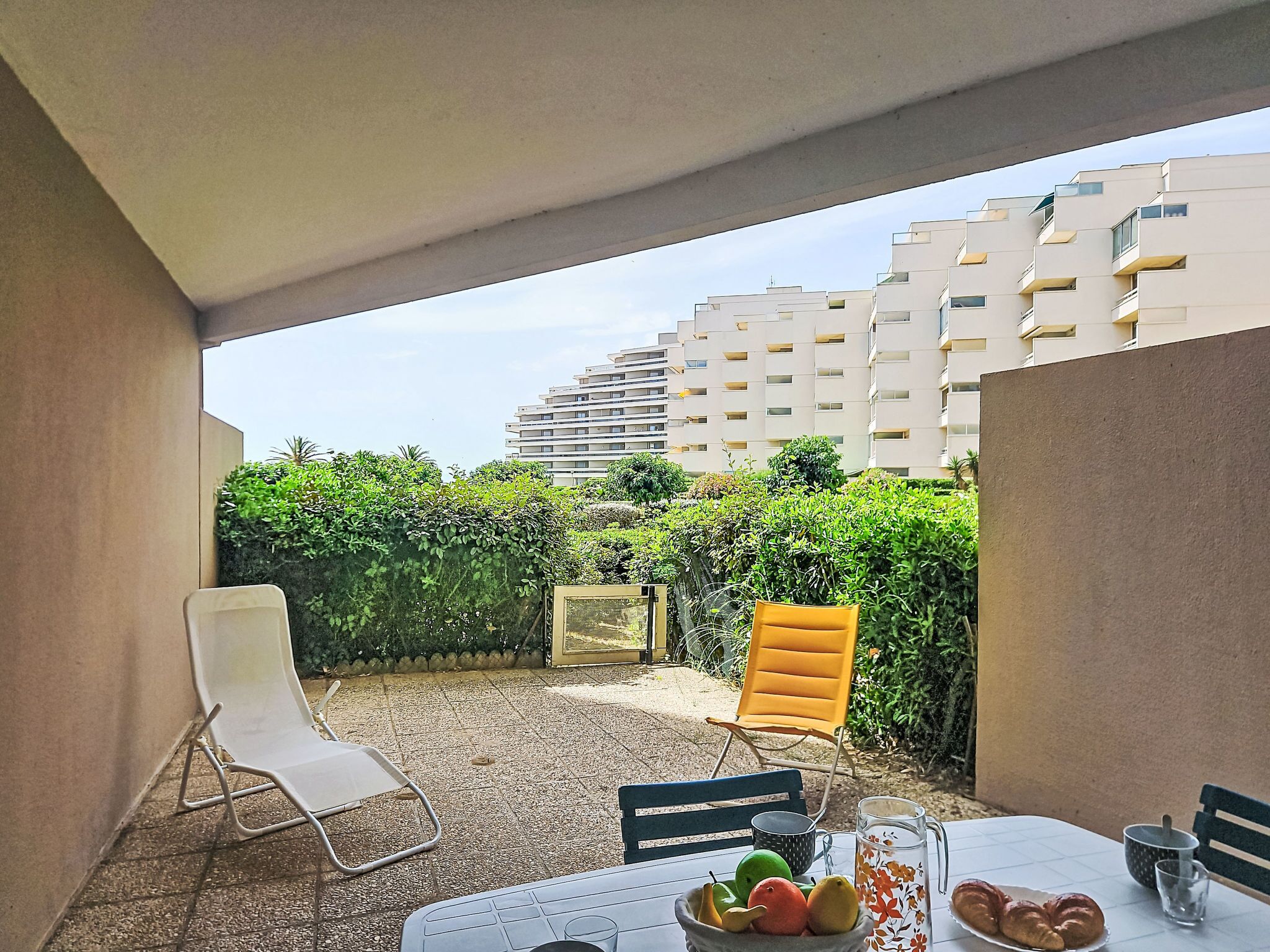Un patio con una mesa dispuesta para comer, una silla, un frutero y una jarrón.